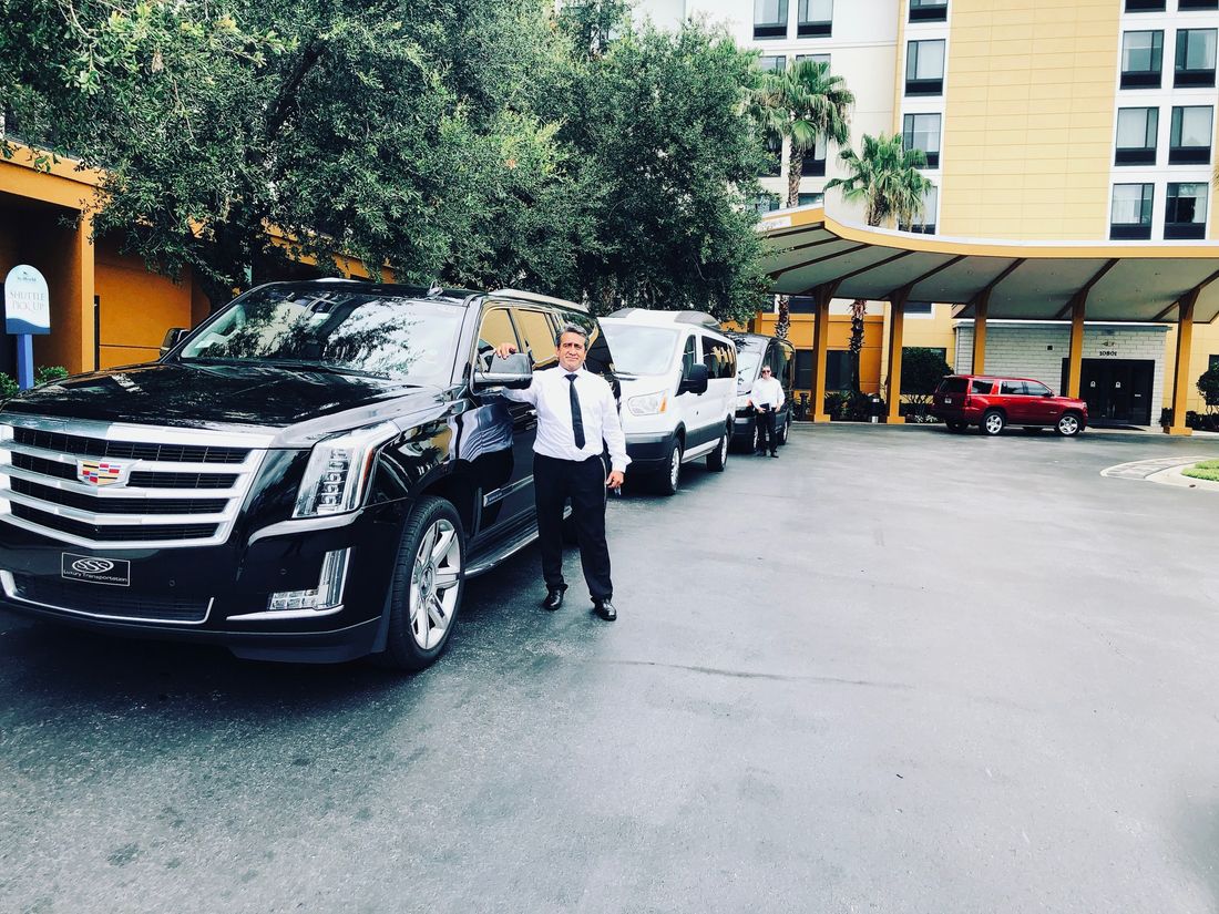 Chauffeurs beside black Escalades